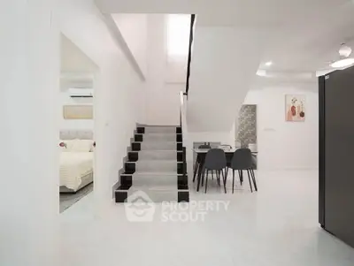 Modern open-plan living area with staircase and dining set, adjacent to a cozy bedroom.