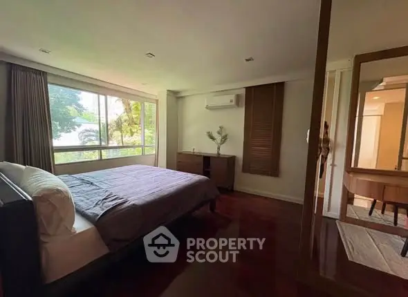 Spacious bedroom with large window and elegant wooden flooring.