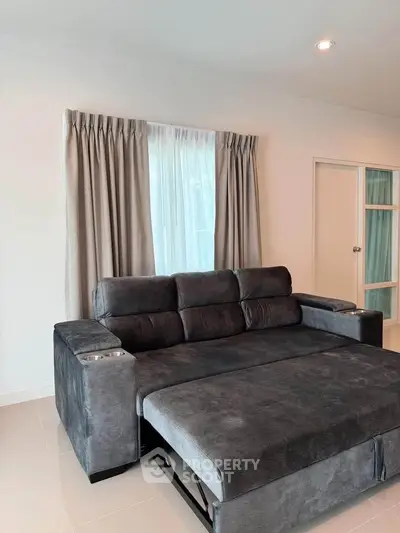 Spacious living room with modern gray sofa bed and elegant curtains.