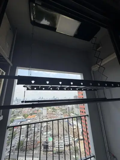 High-rise balcony with cityscape view, featuring laundry drying rack and air conditioning unit.