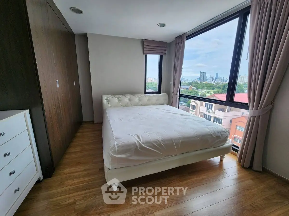 Spacious bedroom with large windows offering stunning city views and elegant wooden flooring.