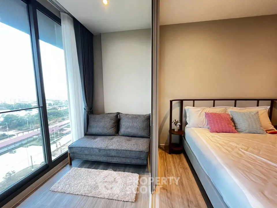 Modern bedroom with large windows and cozy seating area, offering a stunning city view.