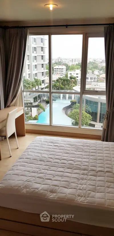 Modern bedroom with large window offering stunning pool and city view in high-rise apartment.