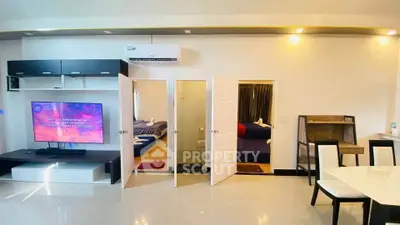 Modern open-plan living room with sleek furniture and two bedrooms, featuring a large TV and dining area.