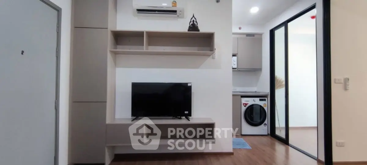 Modern living room with TV and air conditioning, adjacent to a laundry area with washing machine.