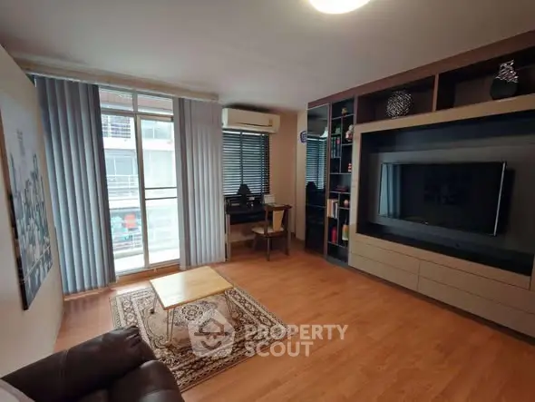 Modern living room with stylish decor, large TV, and natural light from balcony window.