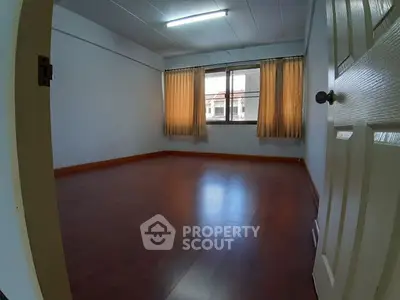 Spacious empty room with wooden flooring and large window, ideal for customization.