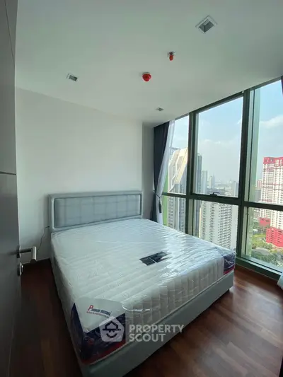 Modern bedroom with large windows offering stunning city views in a high-rise apartment.