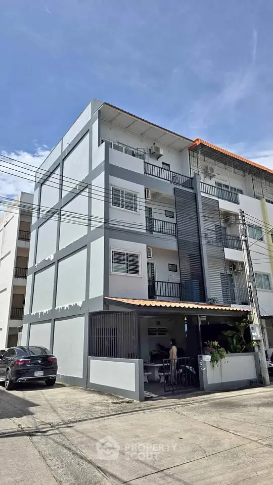 Modern multi-story residential building with balconies and parking area in urban setting.
