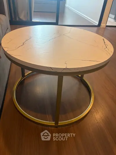 Stylish round marble coffee table with gold metal base on wooden floor