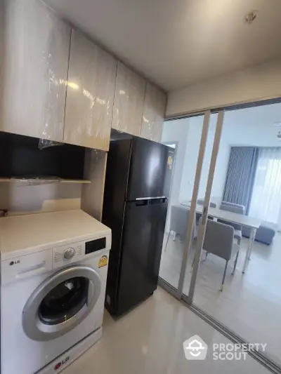 Modern kitchen with sleek appliances and dining area, featuring a washing machine and refrigerator.