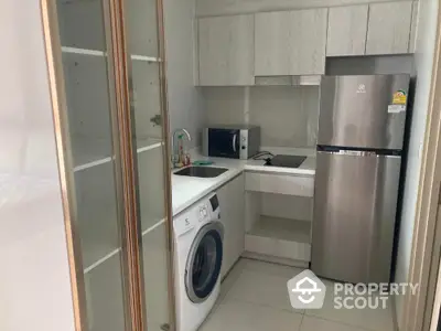 Modern compact kitchen with washing machine and stainless steel fridge in sleek apartment.