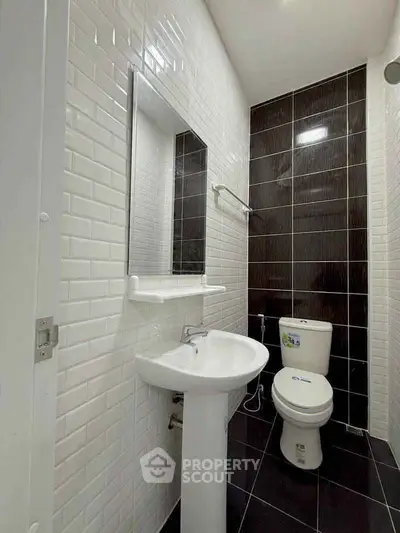 Modern bathroom with sleek black and white tiles, featuring a pedestal sink and toilet.