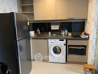 Modern kitchen with sleek appliances including fridge, washing machine, and microwave in compact layout.