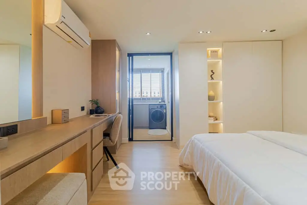 Modern bedroom with built-in desk and view into laundry area, featuring sleek design and ample storage.
