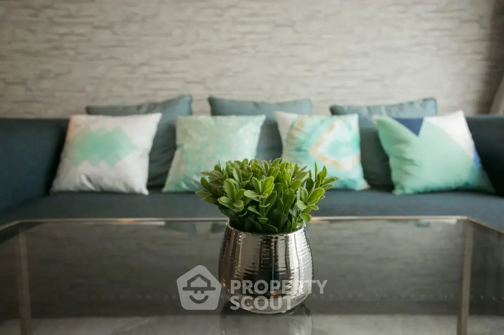 Stylish living room with modern sofa and decorative pillows, featuring a sleek glass coffee table and plant centerpiece.