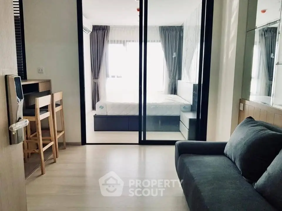 Modern apartment interior with cozy living room and stylish bedroom separated by glass doors.