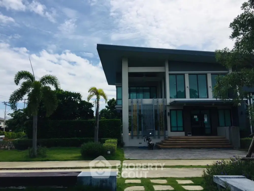 Modern two-story home with expansive glass facade, surrounded by lush greenery and a well-manicured lawn, showcasing contemporary architecture and luxury living.