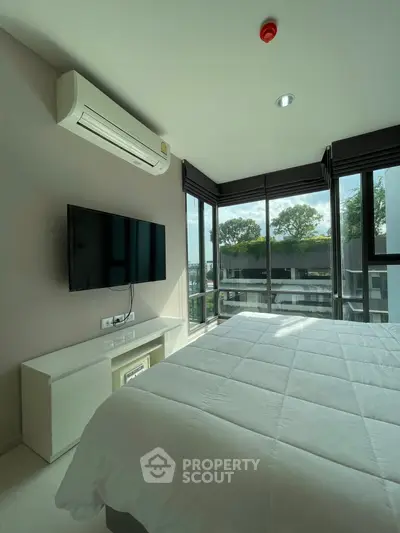 Modern bedroom with large windows and natural light, featuring a wall-mounted TV and air conditioning.