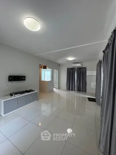 Spacious living room with modern tile flooring and ample natural light, featuring a sleek wall-mounted TV setup.