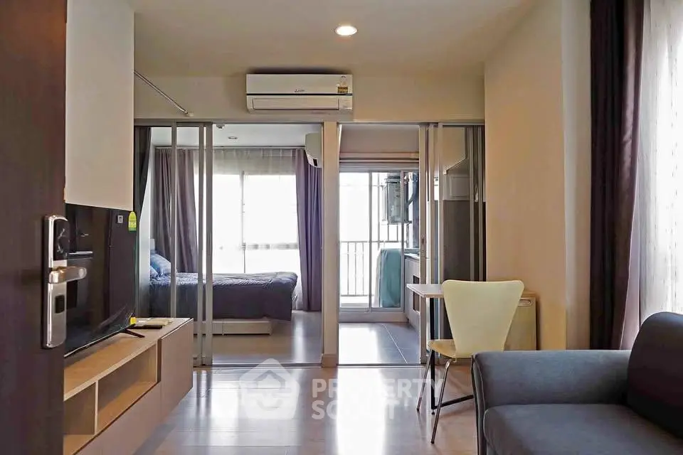 Modern apartment interior with open living room and bedroom, featuring sleek furniture and natural light.