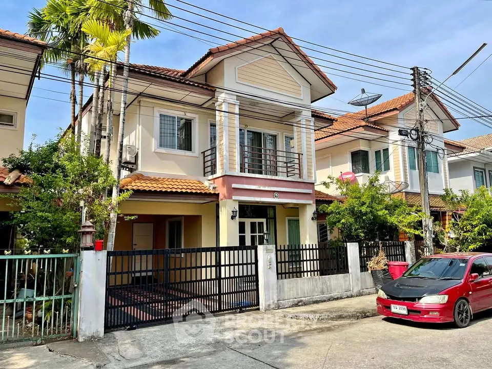 Charming two-story suburban house with gated entrance and lush greenery, perfect for family living.