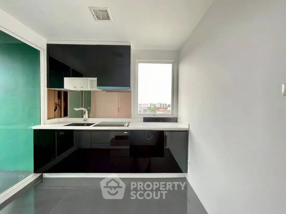 Modern kitchen with sleek black cabinets and large window offering city views.
