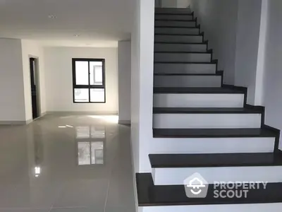 Spacious and modern home interior with glossy tiled floors, elegant black and white staircase leading to the upper level, and ample natural light.