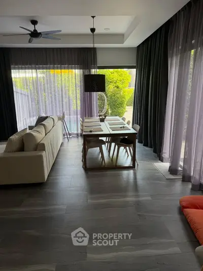 Modern living room with large windows and garden view, featuring elegant dining area and stylish decor.