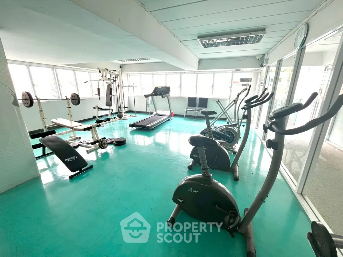 Spacious gym with modern equipment and large windows for natural light.