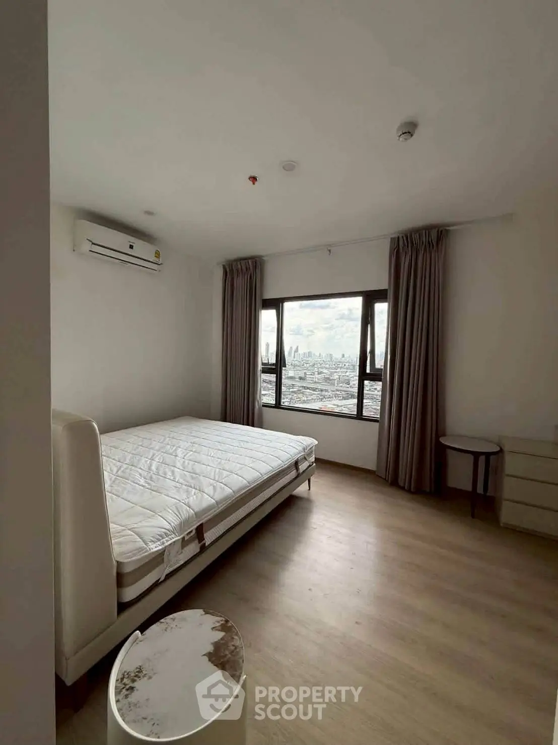 Spacious bedroom with city view, featuring a large window, air conditioning, and modern furnishings.