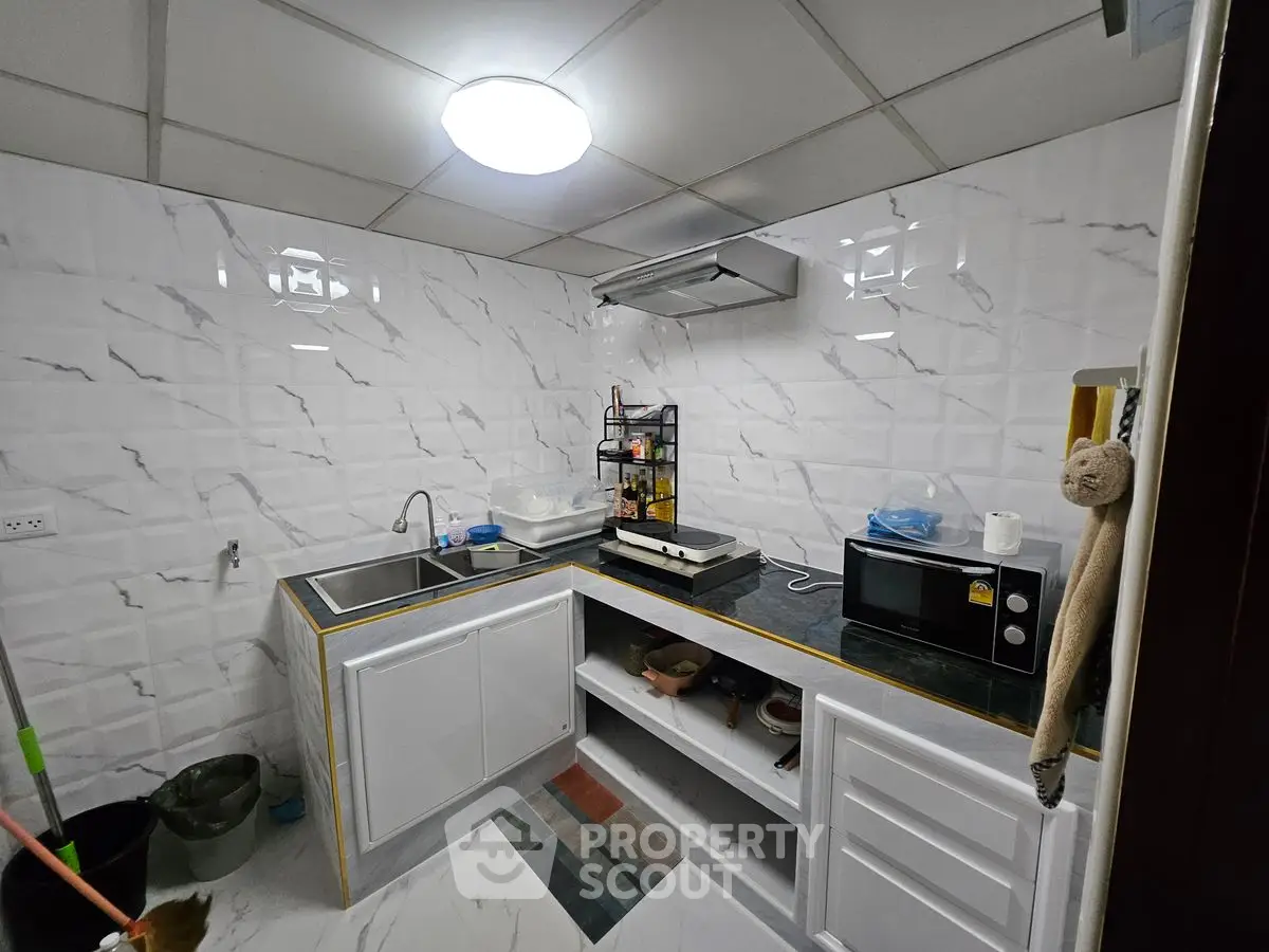 Modern kitchen with sleek white cabinets and black countertop, featuring a microwave and sink.