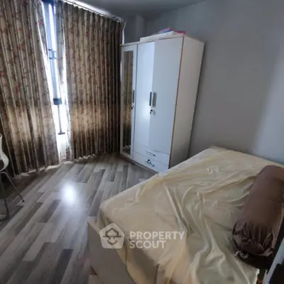 Cozy bedroom with wooden flooring and floral curtains, featuring a bed and wardrobe.