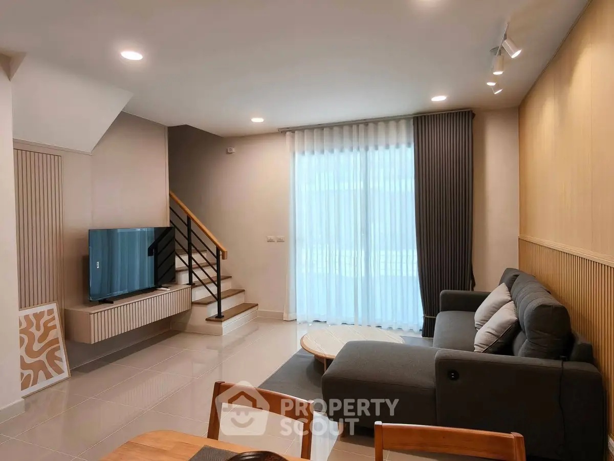 Modern living room with stylish furniture and natural light, featuring a cozy sofa and sleek TV setup.