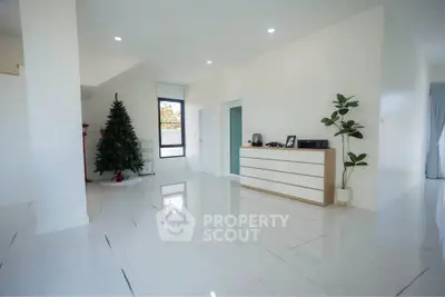 Spacious modern living room with sleek white tiles and minimalist decor, featuring a Christmas tree and natural light.