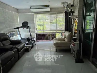 Spacious living room with modern furniture and treadmill, featuring large windows and natural light.