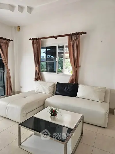 Spacious living room with modern white sofa and glass coffee table, featuring elegant curtains and natural light.