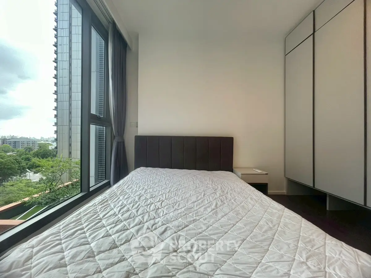 Modern bedroom with large window and built-in wardrobe offering city view.