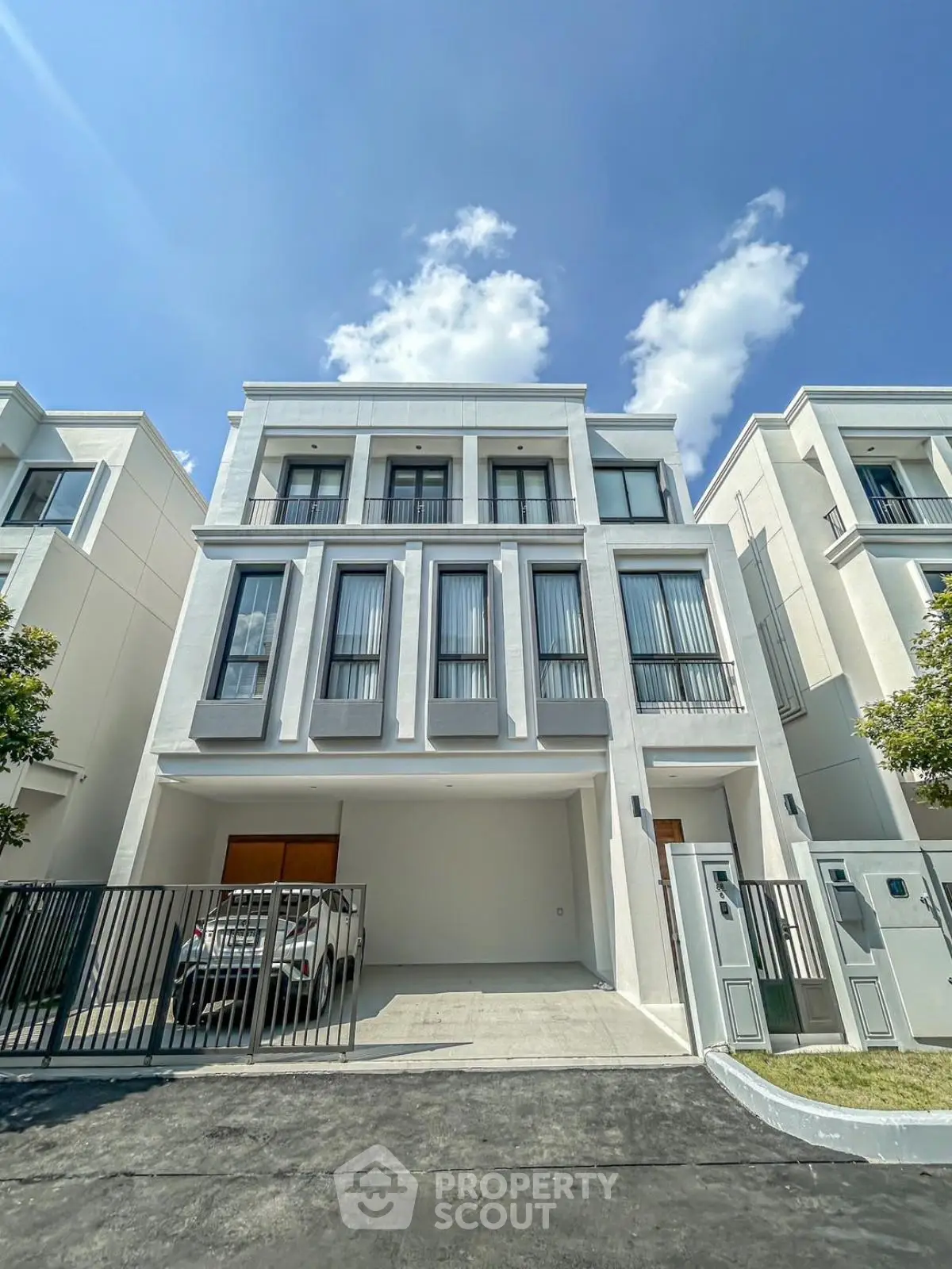 Modern three-story townhouse with sleek facade and spacious driveway under a clear blue sky.