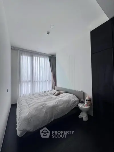 Modern bedroom with large window and sleek black wardrobe, featuring a cozy bed and minimalist decor.