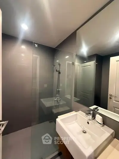 Modern bathroom with glass shower and sleek sink in contemporary apartment.