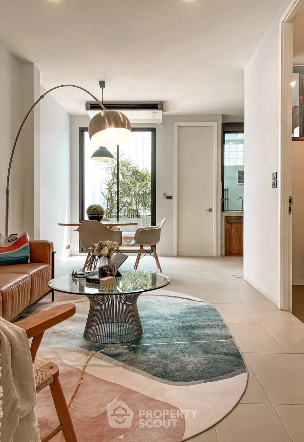 Chic modern living room with elegant furniture and tasteful decor, leading to a sunlit balcony with greenery, showcasing a perfect blend of comfort and style.