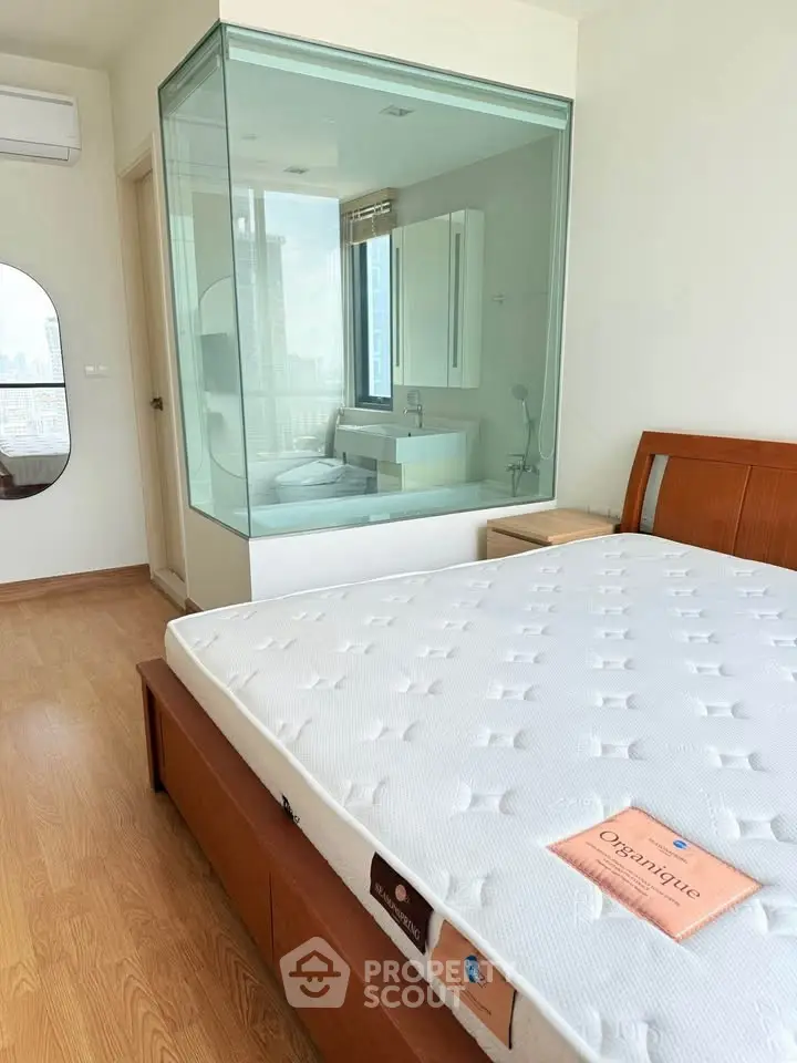 Modern bedroom with glass-enclosed bathroom and city view, featuring a stylish wooden bed and sleek design.