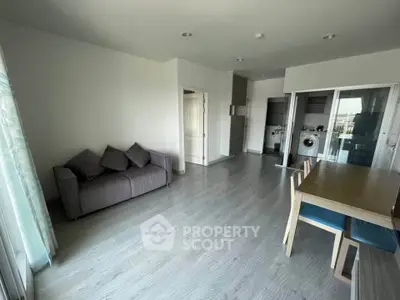 Spacious modern living room with open kitchen and dining area, featuring sleek flooring and natural light.