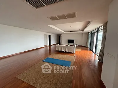Spacious living room with wooden flooring and large windows offering natural light.