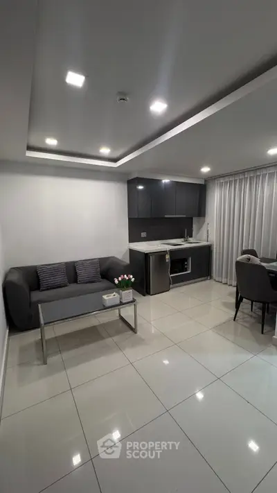 Modern open-layout living room with sleek kitchen and dining area, featuring contemporary furniture and bright lighting.