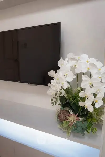 Modern living room with wall-mounted TV and elegant floral arrangement on sleek console.