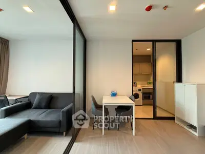 Modern living room with sleek furniture and glass partition leading to a stylish kitchen.