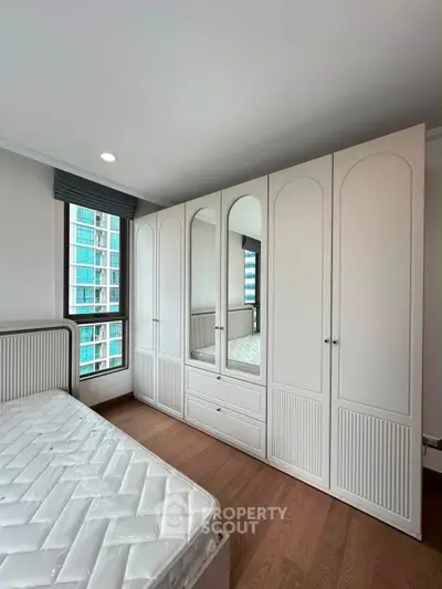 Spacious bedroom with elegant built-in wardrobe and large window view.