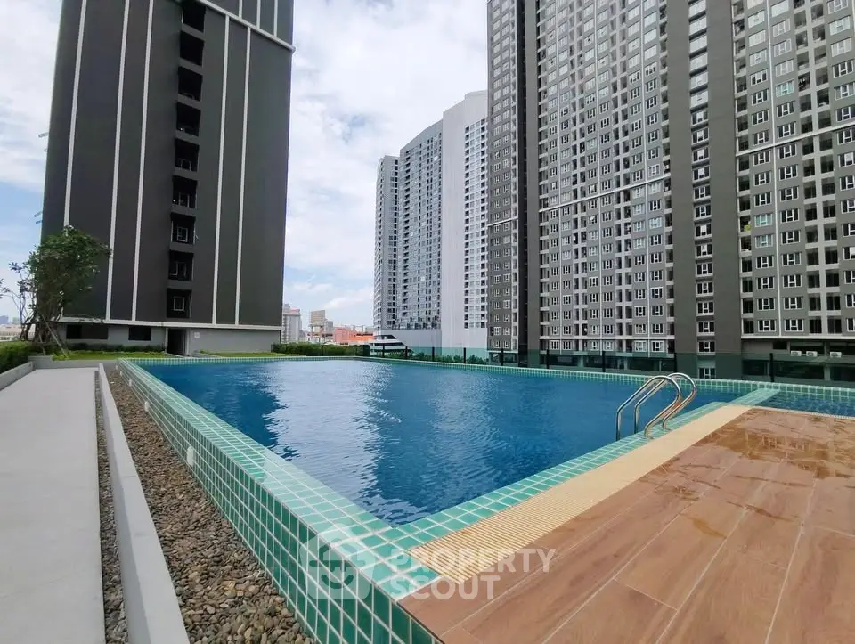 Modern high-rise apartment complex with a luxurious outdoor swimming pool and city skyline view.